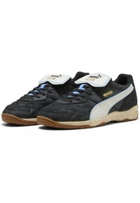 Tênis atléticos pretos com detalhes em branco e azul, parte superior texturizada, sola de borracha, colarinho acolchoado e faixa de Velcro para um ajuste seguro.