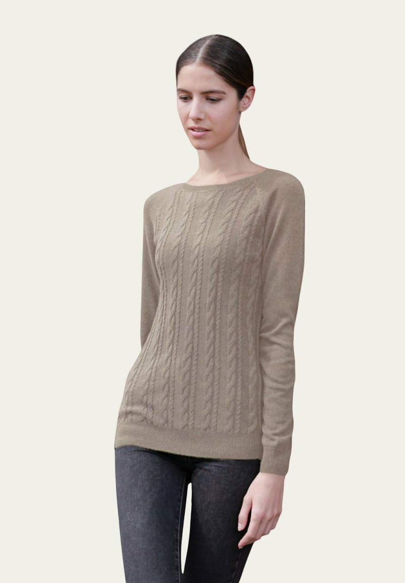 Pull en maille beige avec un col rond et des manches longues, présentant un ourlet côtelé et un motif texturé. Porté par-dessus un jean foncé.