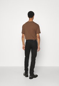 Hnědý tričko s krátkým rukávem, černé slim-fit džíny a černé kotníkové boty. Pozadí je jednoduché bílé, což zdůrazňuje outfit.