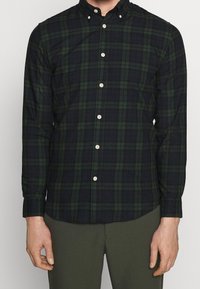 Långärmad rutigt skjorta i mörkgrön och marinblå, tillverkad av bomullsflanell. Har en knapp-down krage och vita knappar fram.