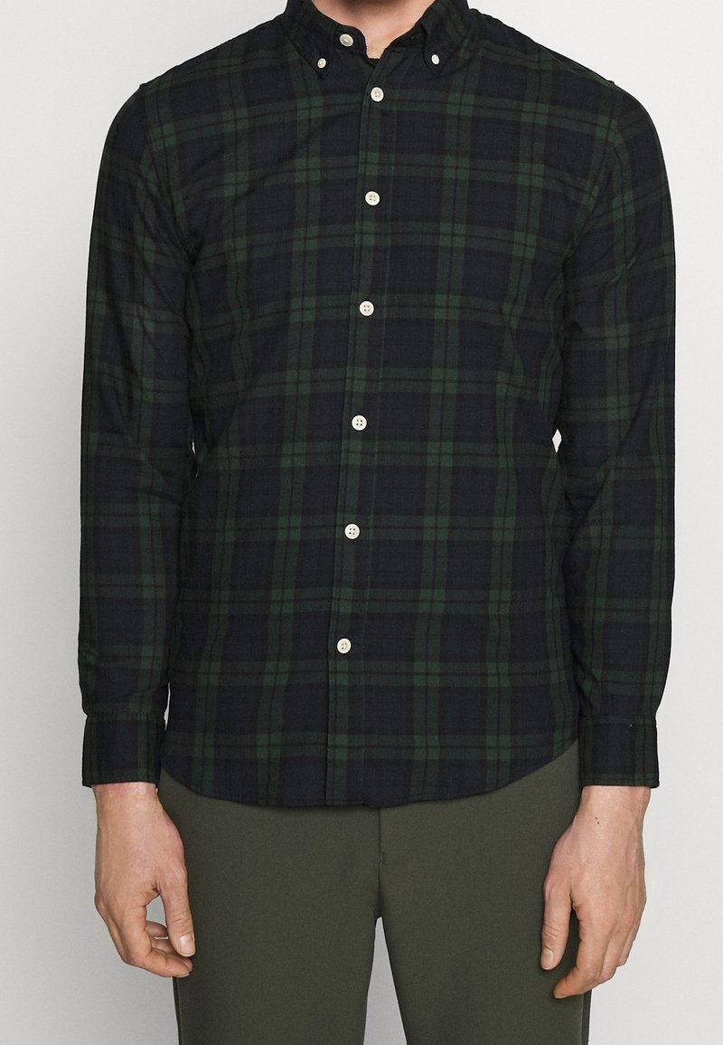 Långärmad rutigt skjorta i mörkgrön och marinblå, tillverkad av bomullsflanell. Har en knapp-down krage och vita knappar fram.