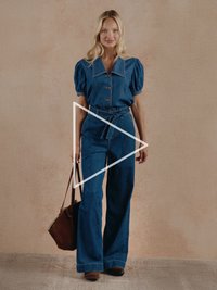 Traper kombinezon s nabranim rukavima, gumbima sprijeda, odgovarajućim remenom i širokim nogavicama. Nošen s smeđom torbom preko ramena i gležnjačama.