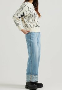 Sweater: krämfärgad med svarta grafiska mönster; löst sittande. Jeans: ljusblå denim, avslappnad passform, uppvikta nederkanter med mönstrad trim, bärs med svarta kraftiga stövlar.