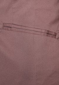 Gros plan d'un tissu marron clair avec une poche fente horizontale et des coutures verticales visibles.