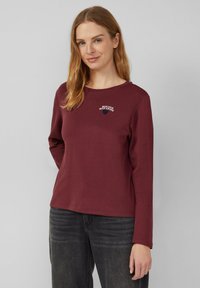Bordeaux farbenes langärmliges Shirt mit Rundhalsausschnitt, das auf der Brust mit kontrastierender Farbe bestickten Text "BONJOUR MON AMOUR" zeigt.