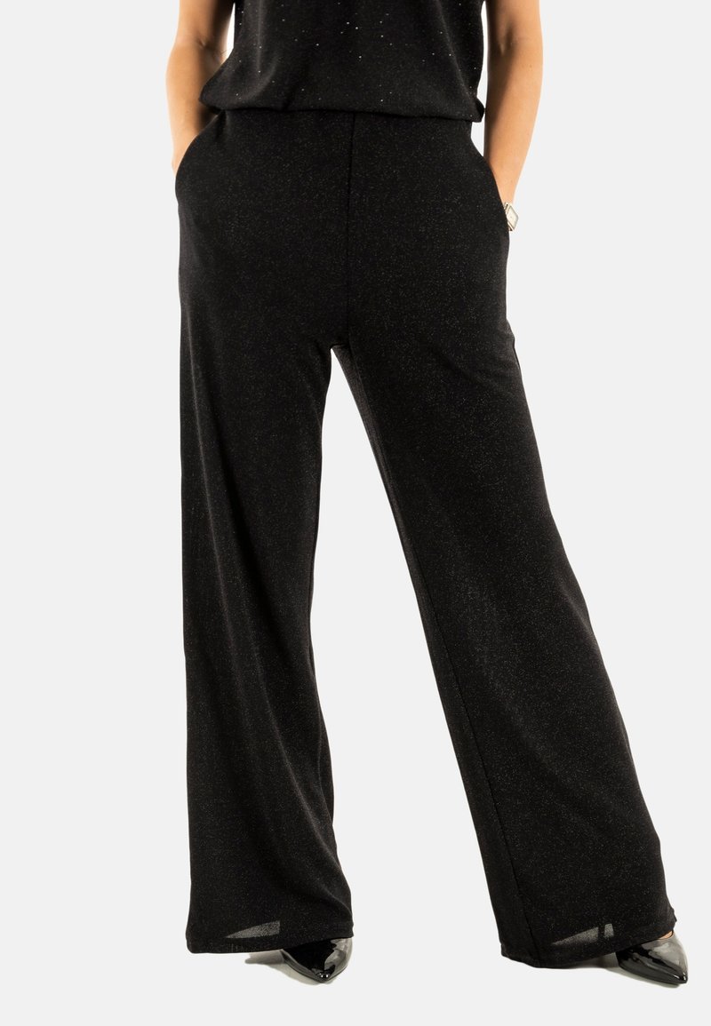 Pantalons larges noirs en tissu texturé avec un léger éclat. Possède des poches latérales et une coupe décontractée. Convient à diverses occasions.