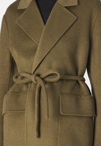 Abrigo de lana verde oliva con cuello chal, cinturilla y dos grandes bolsillos aplicados. Textura suave y corte clásico.
