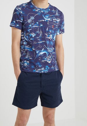 Granatowa bawełniana koszulka z tropikalnym nadrukiem przedstawiającym niebieskie i białe żaglówki, ryby oraz palmy. Okrągły dekolt i krótkie rękawy.