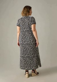 Maxiklänning med svartvit lövdesign, korta ärmar, rund halsringning och sidoflikar; matchad med svarta kilklackar.