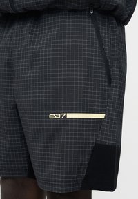 Μαύρο σορτς με λεπτό λευκό πλέγμα, πλαϊνή τσέπη με φερμουάρ και λογότυπο "ea7" με οριζόντια μπεζ ρίγα στο μηρό.