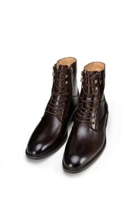 Hnědé kožené kotníkové boty s šněrovacím designem, mosaznými detaily a vyšitými prvky. Hladký povrch s špičatou špičkou.