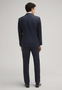 Abito blu marino con silhouette su misura, rever a punta e pantaloni slim-fit. Texture liscia, design minimalista e dettagli di cucitura sottili.