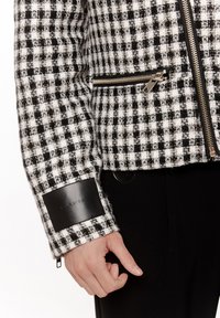 Czarna i biała kurtka w kratę z fakturowanej tkaniny, z srebrnymi suwakami, czarnym skórzanym akcentem na mankiecie i dopasowanym krojem.