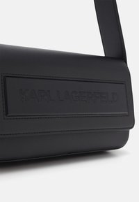 Zwarte lederen handtas met een rechthoekige vorm, voorzien van een reliëflogo, een gladde textuur en een platte draagband.