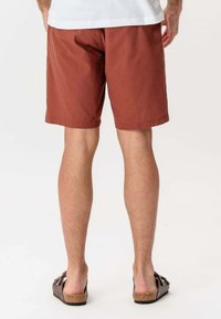 Rustrøde shorts lavet af bomuld med et enkelt design. Bæret med brune sandaler, der eksponerer benene og sikrer komfort.