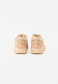 Bež suede tenisice s mrežastim detaljima, zaobljenim stražnjim dijelom i teksturiranim potplatom. "Saucony" je utisnut na peti. Svijetla neutralna paleta boja.