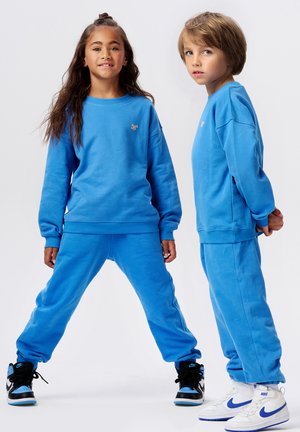 Blaue passende Sweatshirt und Jogginghose, mit gerippten Bündchen und Rundhalsausschnitt. Weiße und schwarze Sneakers mit blauen Akzenten runden den Look ab.