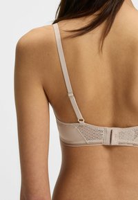 Beige rintaliivi, jossa on pitsiyksityiskohtia, säädettävät olkaimet ja hakassuljenta takana. Silkinpehmeä kangas ja minimalistinen muotoilu.