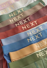 Pino värikkäitä kangasvyönauhoja, joihin on painettu kullalla "NEXT"-merkkilogo, järjestetty vaakariveihin.