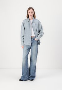 Lyseblå denimskjorte med avslappet passform og knappestolpe, lagd over en hvit crop top og kombinert med vide blå jeans.