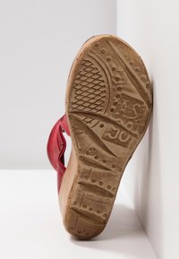 Sandale rouge avec un talon en bois et une semelle en caoutchouc texturée. Elle présente un dessus en cuir lisse et un motif de relief bien défini sur la semelle. Taille 37.