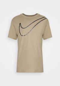Světle hnědé bavlněné tričko s velkým černým logem Nike swoosh a textem "Just do it" v světlejším odstínu. Krátké rukávy a kulatý výstřih.