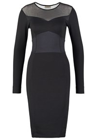 Svart klänning med långa ärmar och transparent meshyoke. Har en figurnära silhuett, kontrasterande ogenomskinliga paneler och en knälång fåll.