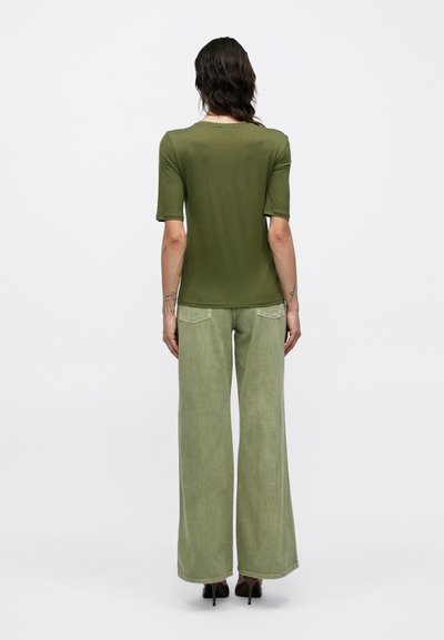 Tricou verde măsliniu mulat, cu mâneci scurte, asortat cu blugi verzi cu picioare largi. Ținuta are un design simplu și o textură moale.