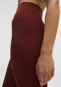 Vysoké legíny v burgundskej farbe, vyrobené z hladkého a elastického materiálu. Obsahujú bočnú kapsu a ploché švy pre zvýšenú odolnosť.