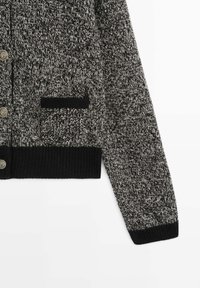 Cardigan en tricot noir et blanc chiné avec poignets et ourlet côtelés noirs, poche avant avec bordure noire et boutons décoratifs argentés.