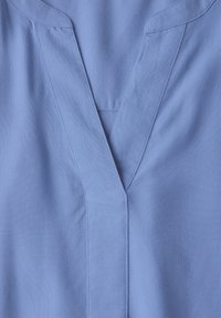 Haut bleu clair en V fabriqué à partir d'un tissu tissé lisse avec une texture subtile. Il présente un design simple et épuré avec des coutures détaillées.