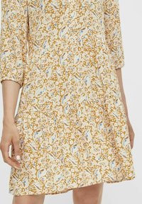 Gelbes Blumenkleid mit Dreiviertelärmeln, einem gestuften Saum und einem Stoff mit aufwendigen Paisley- und Blattmustern in Creme und Blau.