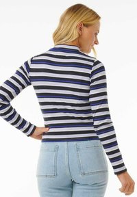 Langärmliges gestreiftes Oberteil mit schwarzen, grauen und blauen horizontalen Streifen; gerippte Textur; figurbetontes Design; hoher Kragen; kombiniert mit hellblauen Jeans.