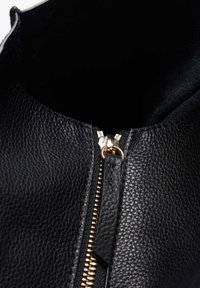 Chaqueta de cuero negra con acabado texturizado y detalles de cremallera dorada en el frente. El interior parece oscuro y sin adornos.