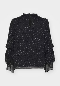 Blouse noire manches longues à pois blancs, col montant volanté, manches à étages et fermeture par bouton goutte d'eau au dos.