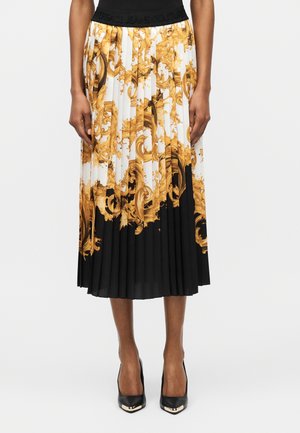 Spódnica plisowana o długości do połowy łydki z złotym barokowym wzorem na białej górnej części i czarnej dolnej części, noszona z czarnymi szpilkami z ostrym noskiem.