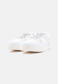 Ζευγάρι λευκά αθλητικά παπούτσια χαμηλού προφίλ με ανοιχτό γκρι κορδόνια και υφασμένα πλαϊνά πάνελ σε απλό λευκό φόντο.