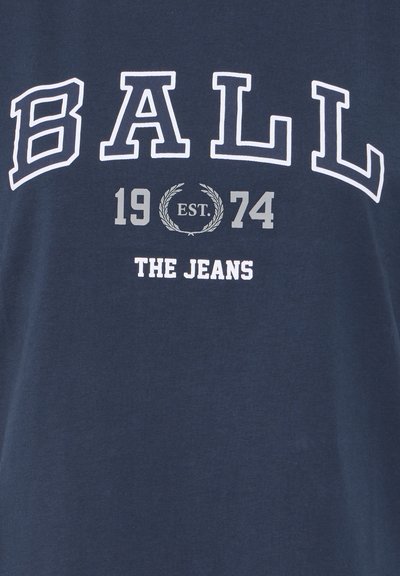 Tricou din bumbac bleu marin cu text alb și gri: "BALL 1974 EST." cu o ramă decorativă de lauri și "THE JEANS" dedesubt.