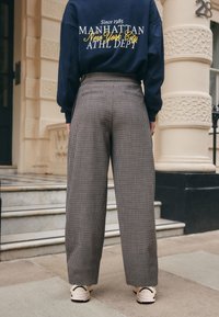 Navy sweatshirt with text, paired with high-waisted, wide-leg trousers featuring a brown and cream houndstooth pattern and cream sneakers.