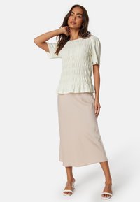 Blusa bianca strutturata con maniche a sbuffo, abbinata a una gonna midi aderente beige. Sandali con tacco trasparente completano l'outfit.