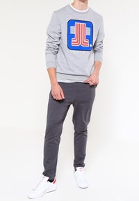 Sudadera gris con un logotipo gráfico azul y rojo en el frente, combinada con pantalones de chándal en color carbón y zapatillas blancas con acentos rojos.