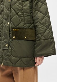 Pihe- és zöld színű dzseki arany színű fém díszítéssel, texturált kordbársony zsebbel, amelyen a márkanév szerepel. Az ujjai bővülő kialakításúak.