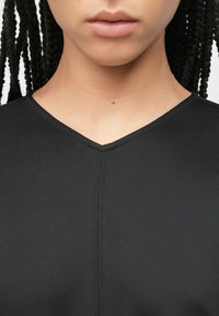 Μαύρο μπλουζάκι με V-λαιμόκοψη και λείο υλικό, με διακριτική ραφή κατά μήκος της λαιμόκοψης και του ώμου.