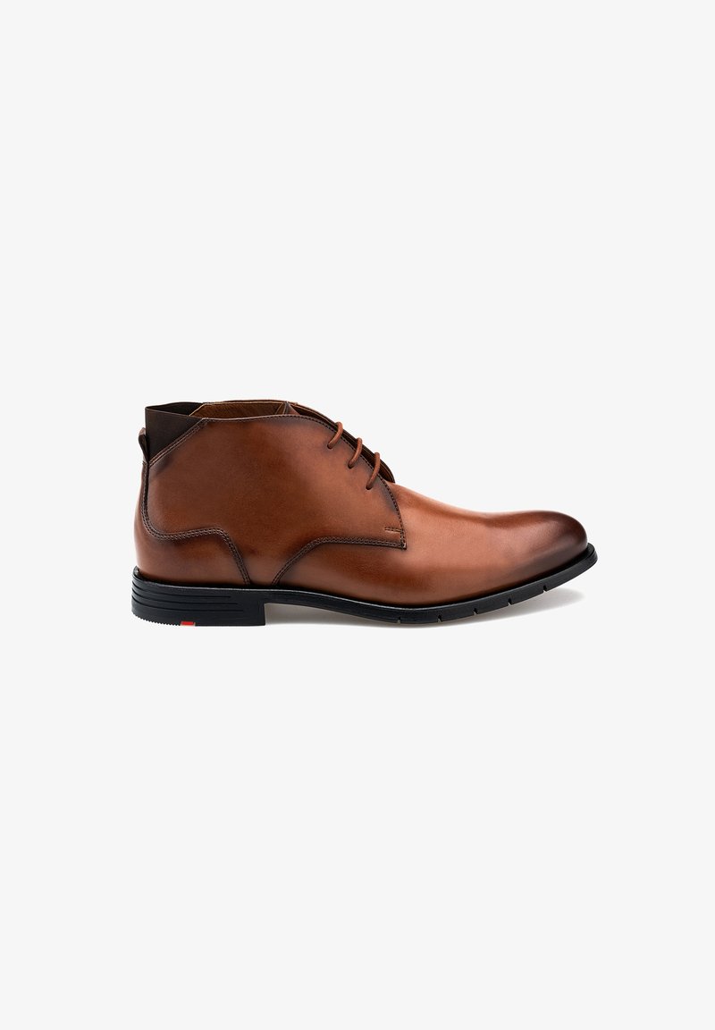 Braune Leder-Chukka-Stiefel mit glatter Oberfläche, runder Zehenform, Schnürdesign und schwarzer Gummisohle mit rotem Akzent an der Ferse.