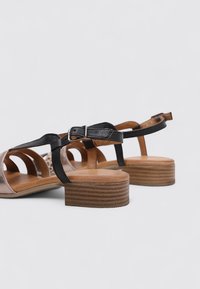 Sandales à talons noirs et bruns avec un talon en bois, comportant des lanières en cuir et des designs découpés. Détail de boucle ajustable sur la lanière.