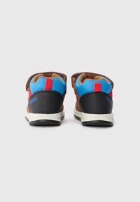 Vue arrière de chaussures d'enfant marron, bleues et rouges avec un col rembourré, une sangle Velcro et une semelle en caoutchouc noir, arborant un détail de logo.