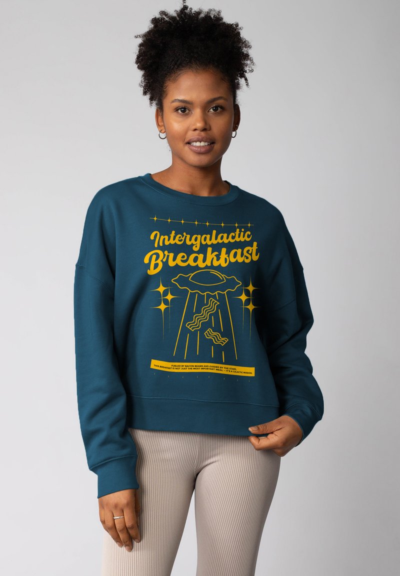 Teal sweatshirt met een grafische print met de tekst "Intergalactic Breakfast" en gele accenten. Casual fit, ronde hals, ribgebreide manchetten.
