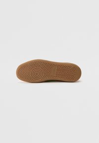 Semelle de chaussure avec un design en caoutchouc texturé de couleur beige. Comprend des motifs circulaires et ondulés pour la traction et la stabilité.