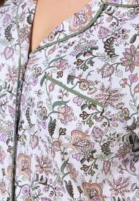 Noční košile s květinovým vzorem vyrobená z lehkého materiálu, obsahující zelené, fialové a růžové barvy. Mezi výrazné detaily patří náprsní kapsa a kontrastní lemování.