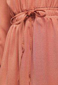 Vestido color melocotón con cintura fruncida y un lazo a juego. Tela ligera y suave con secciones translúcidas y un sutil relieve.
